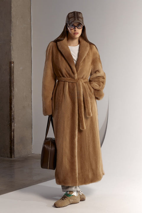 A woman wears a full-length mink fur coat in a rich, natural tone, showcasing timeless elegance and luxurious warmth.