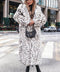 Woman wearing JOVANNA long premium white leopard print faux fur coat, styled with black boots and a chic hat in a city setting.