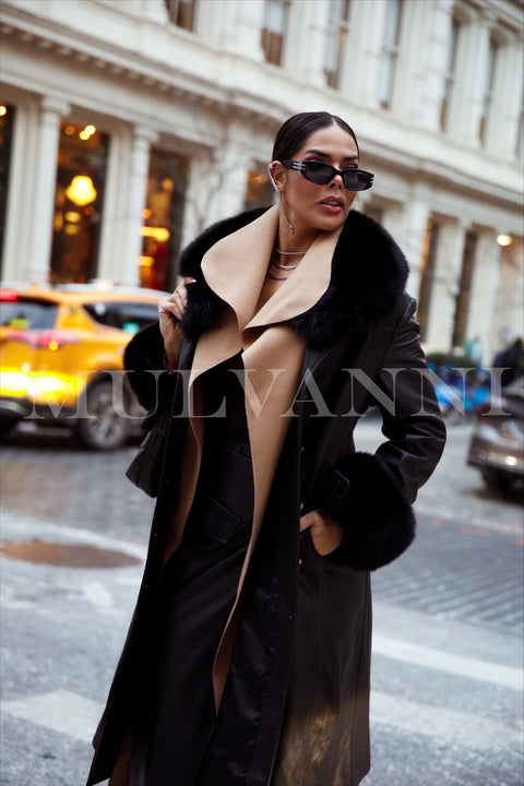 A woman steps out in a black leather trench coat, accented by a large black fox fur collar and cuffs. The combination of leather and fur adds a luxurious touch to her polished outfit.