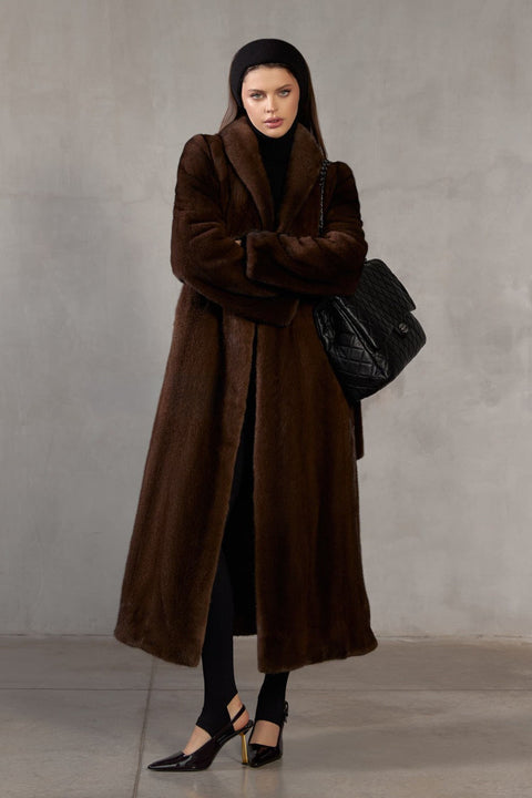 Wrapped in luxurious dark brown mink, a woman showcases timeless sophistication in a gracefully draped long coat.